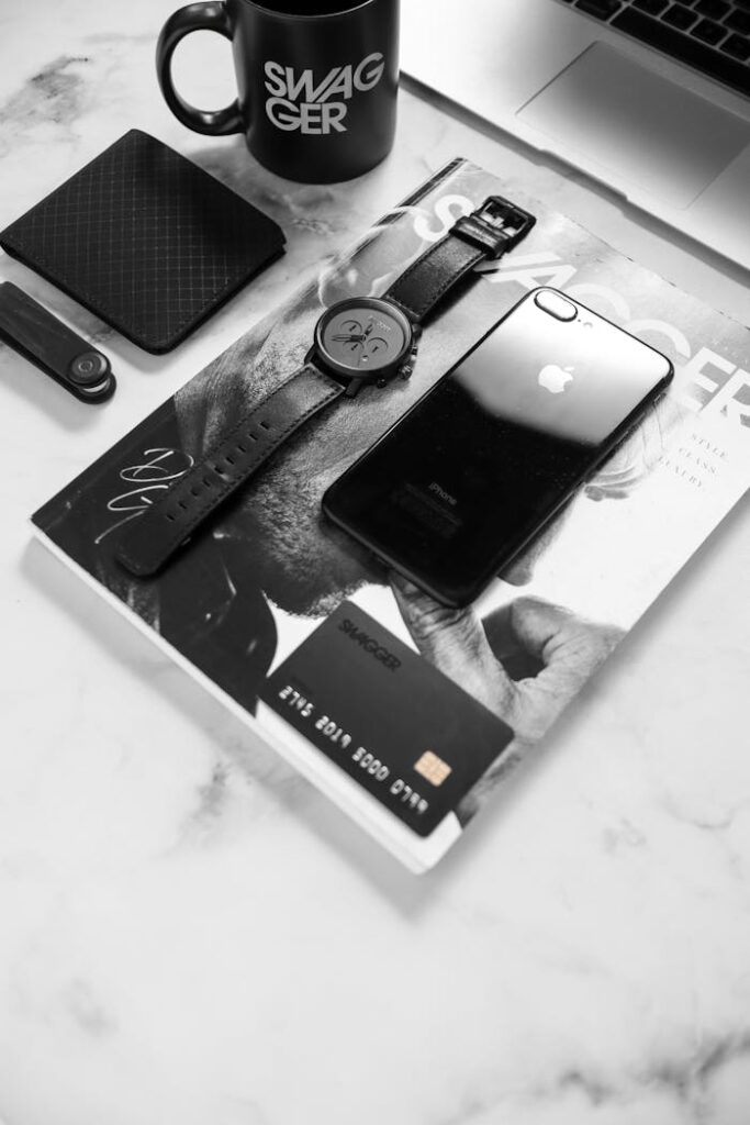 Black and white flat lay showcasing a stylish desk with phone, watch, and accessories.